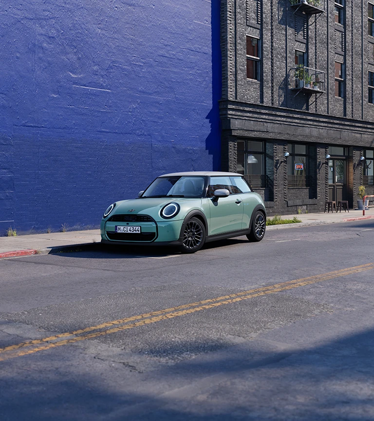 MINI Cooper in Ocean Wave Green parked on an urban street beside a blue wall.