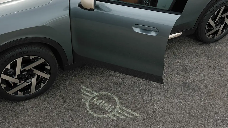 Надворешен поглед на MINI Countryman со отворена врата и MINI логото за добредојде светло на теренот