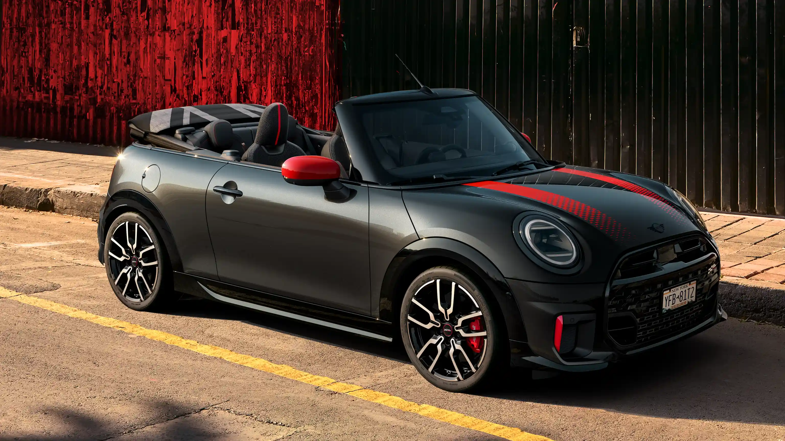 MINI Convertible John Cooper Works in Midnight Black II with Chili Red accents parked on an urban street with the roof down.
